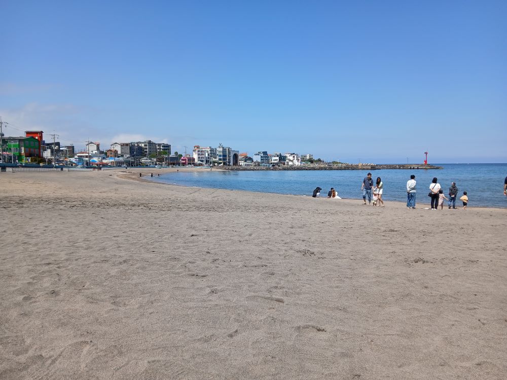 Wide view of Iho Tewoo Beach in Jeju City with buildings in the distance and the ocean on the right